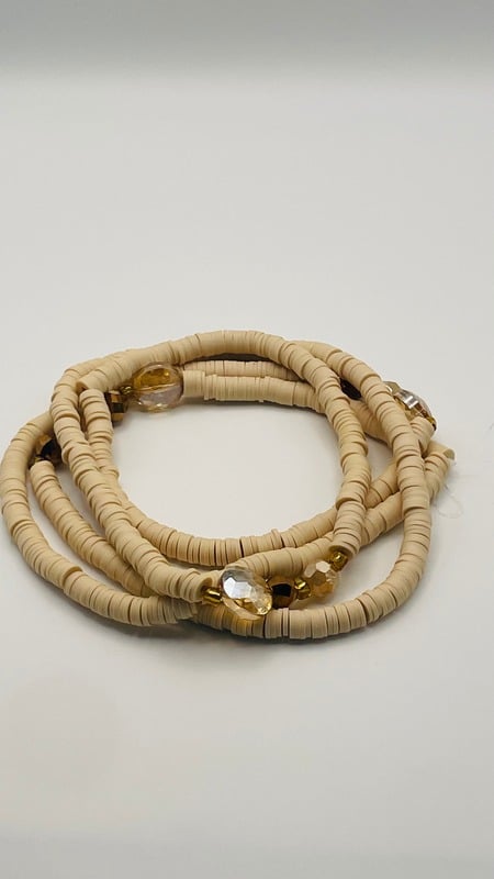 Cream and gold African waist beads with faceted glass accent beads, coiled on a neutral background