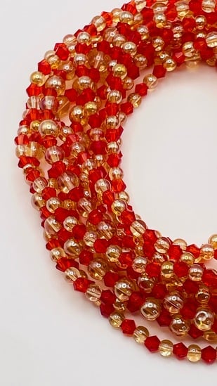 Handcrafted red and gold glass bead African waist beads, coiled on a neutral background