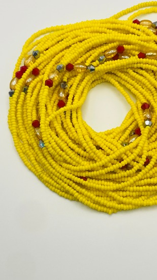 Sunshine yellow African waist beads with red accent beads, coiled on a neutral background